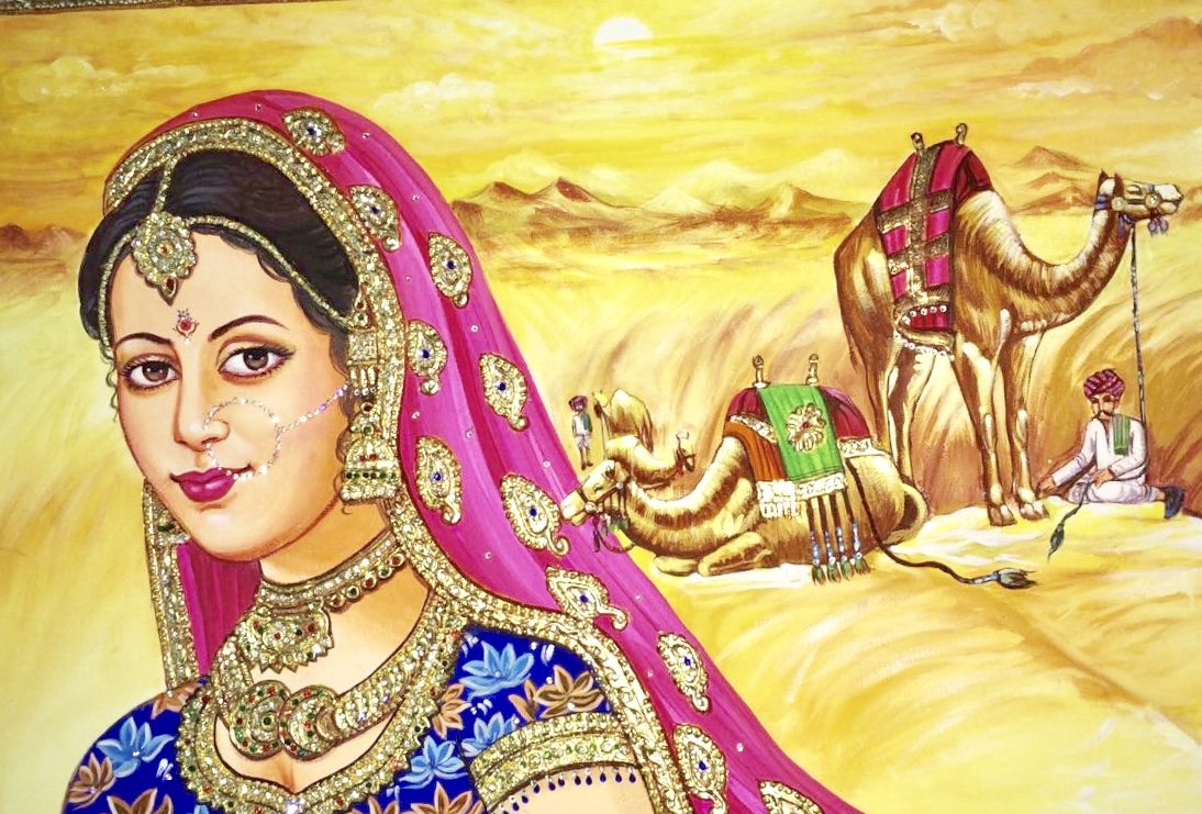 Rajasthani bride in an ornate pink veil with camels crossing the desert behind her